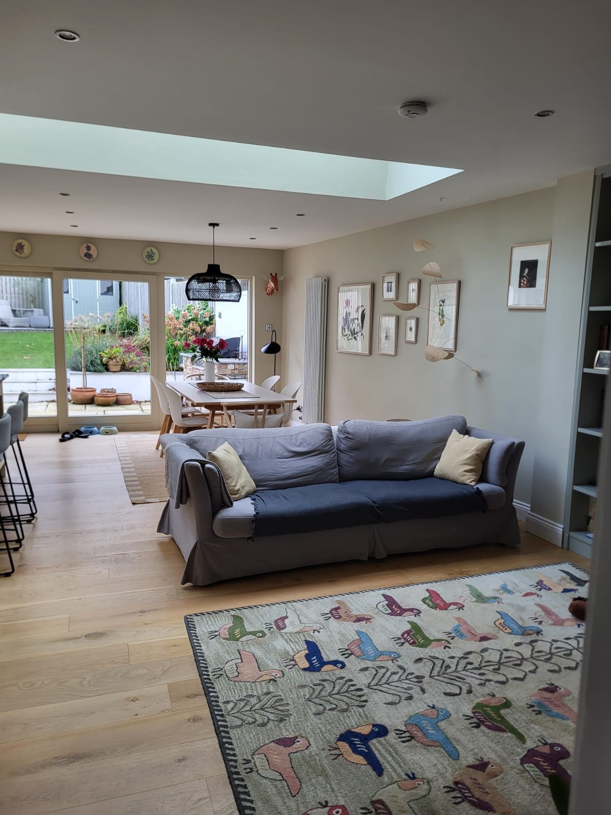 Spacious open-plan living room with blue sofa, wooden dining table, large glass doors to garden, and skylight