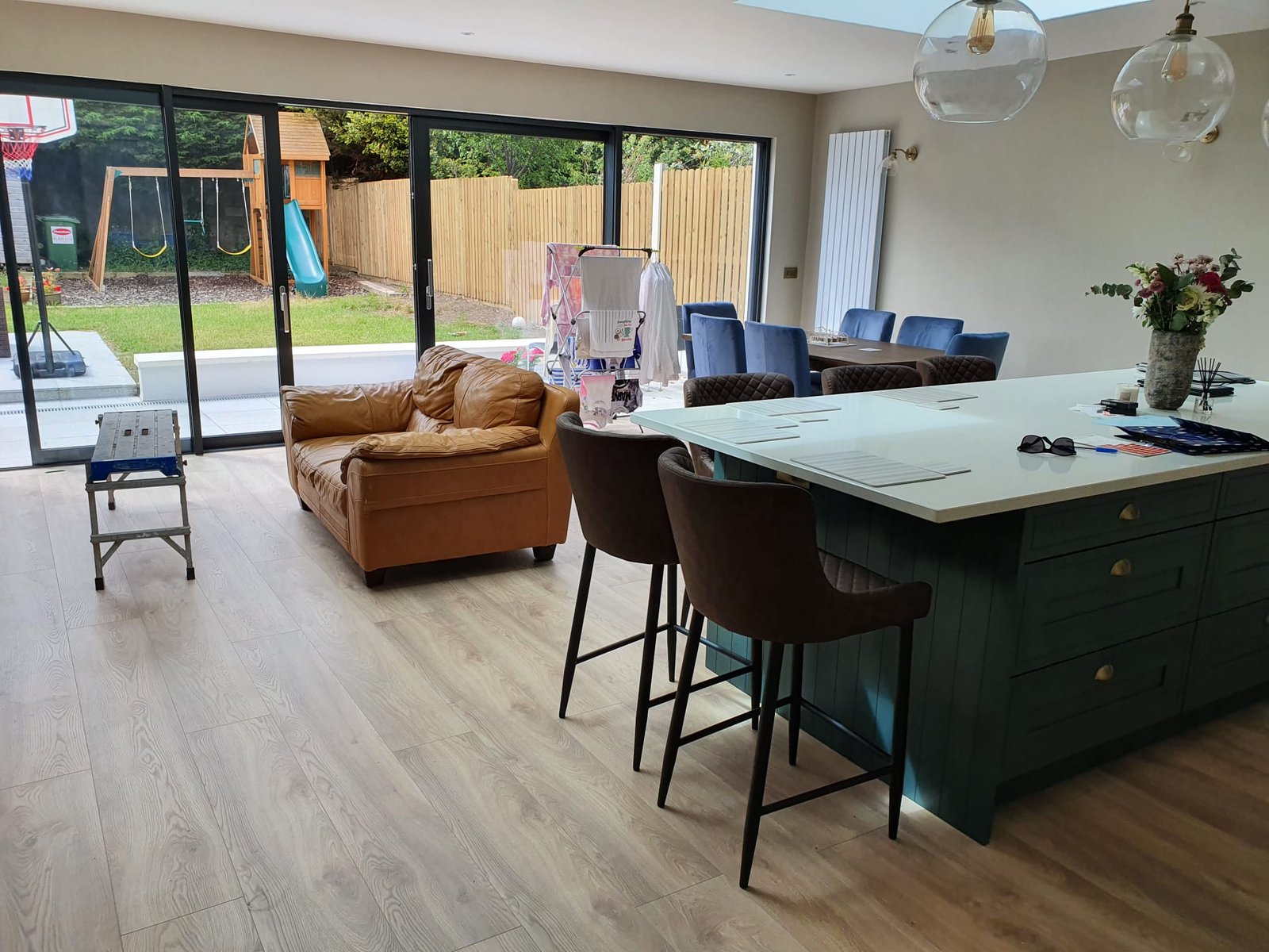 Open-plan kitchen and living area with dark green island, brown leather sofa, and large glass doors to garden