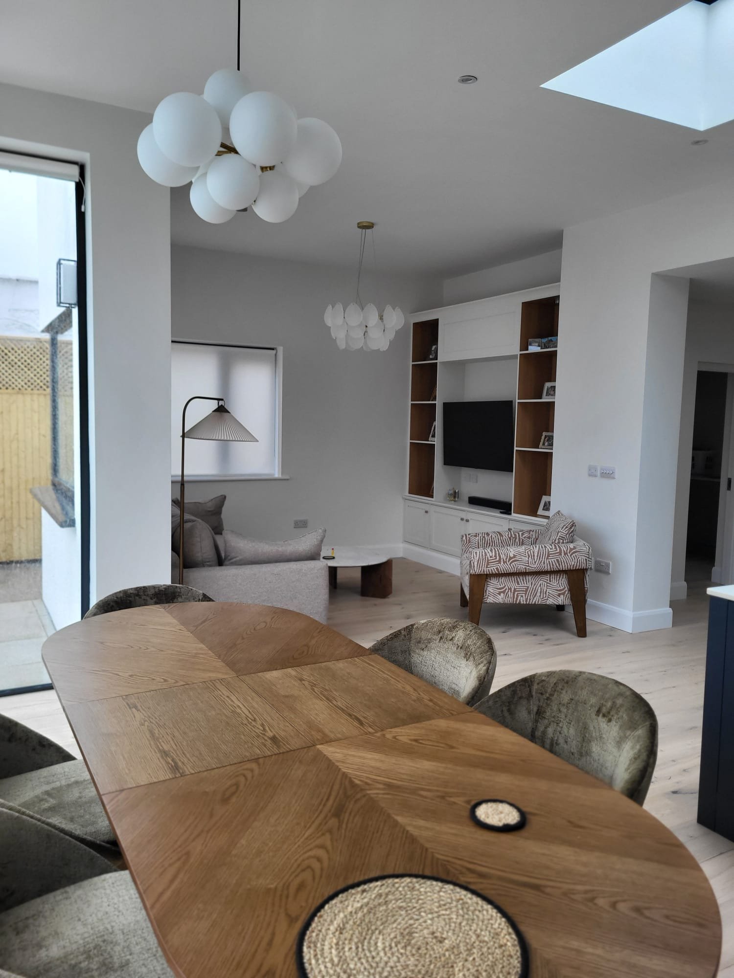Modern living room with white pendant lights, wooden dining table, patterned sofa, and built-in shelving