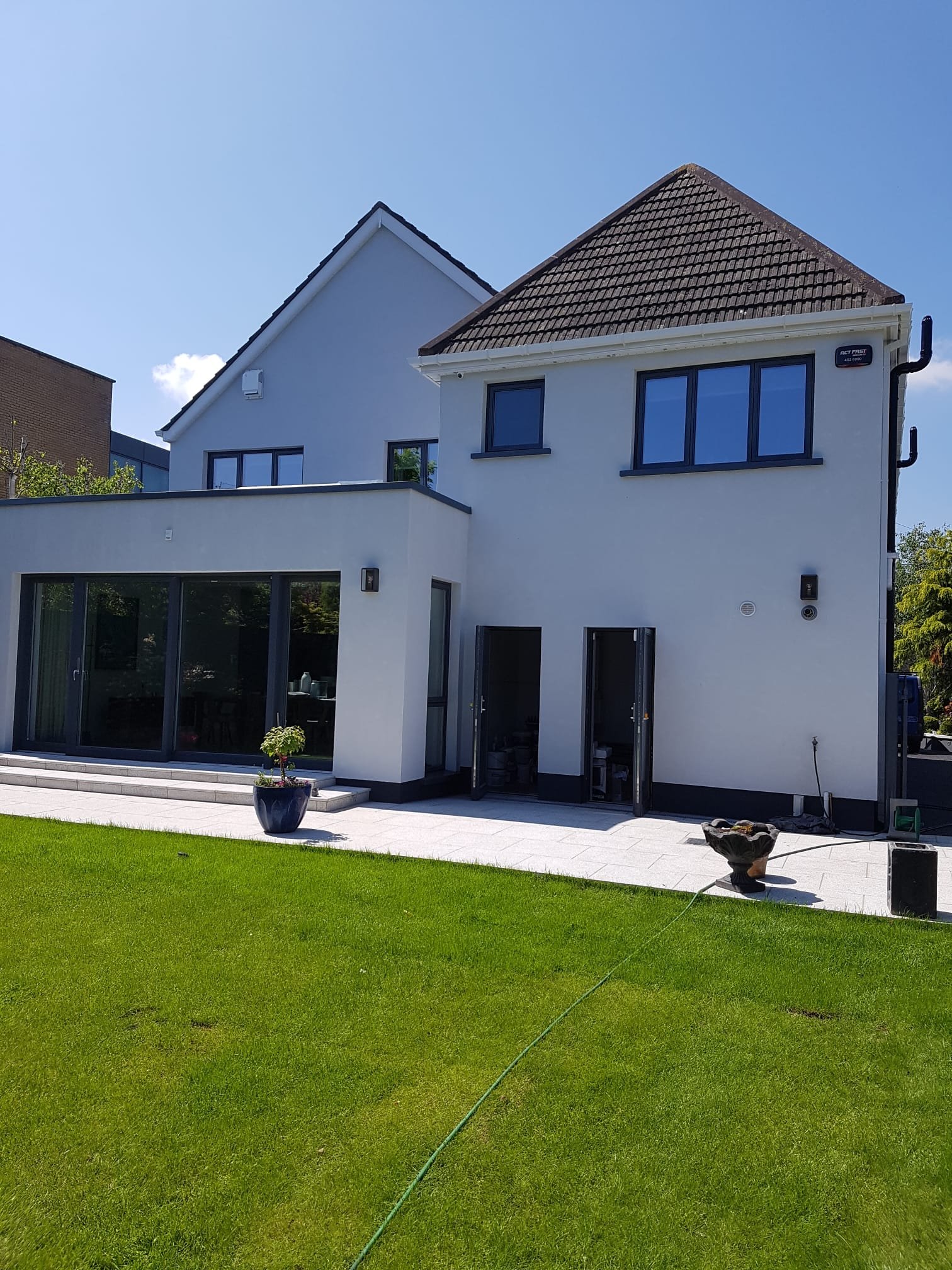 Modern house exterior with white render, black-framed glass doors, and patio