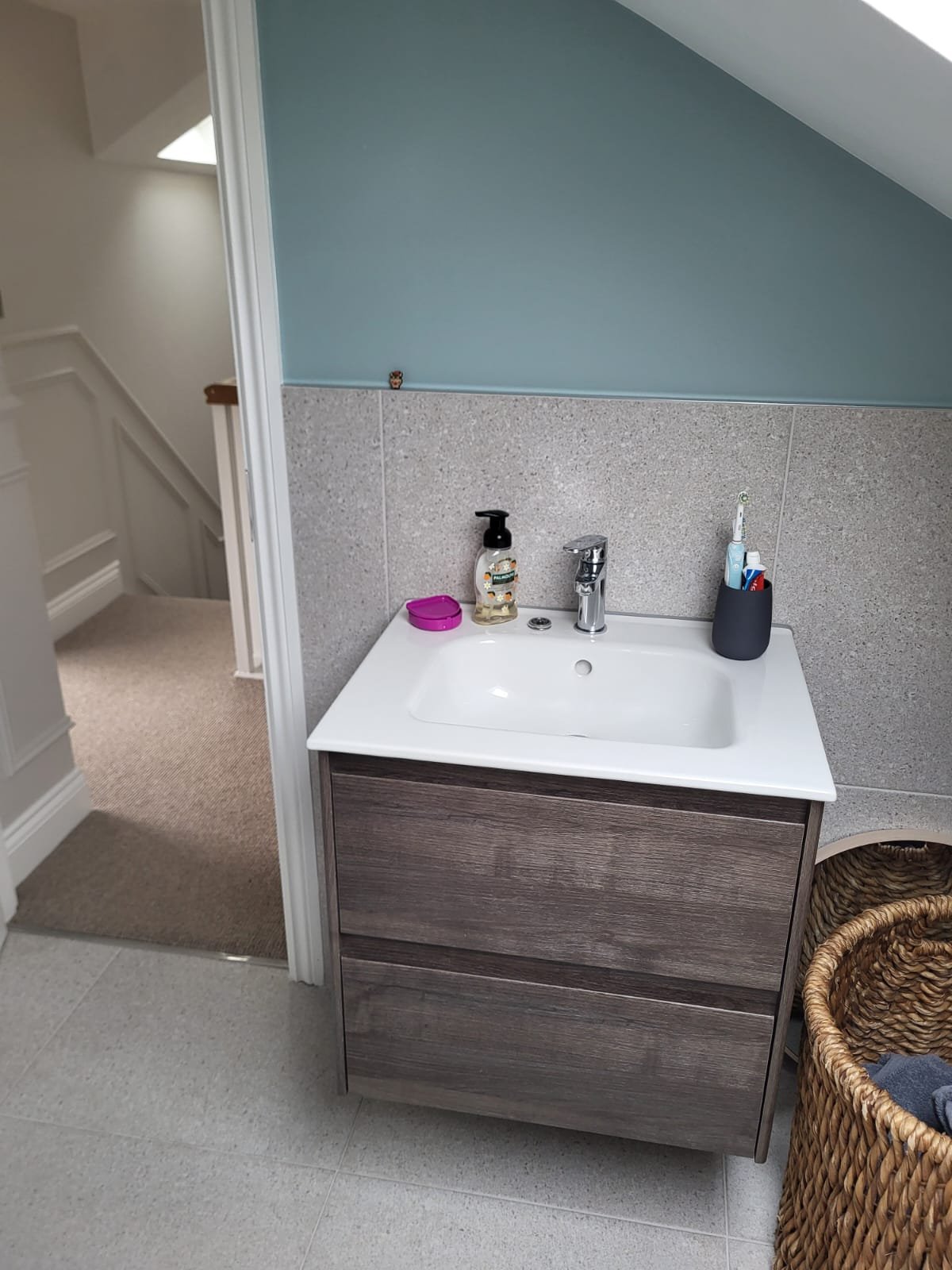 Modern bathroom with dark teal wall, gray tile, dark wood vanity with white sink, and round mirror