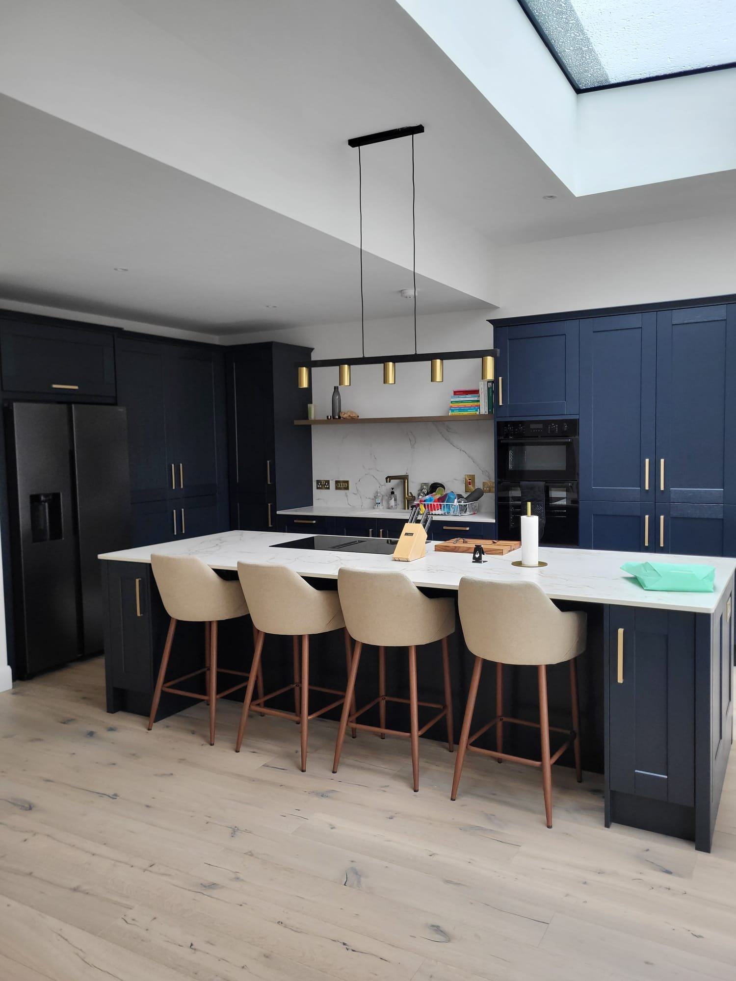 Dark navy kitchen with white marble countertops, cream bar stools, and brass pendant lights