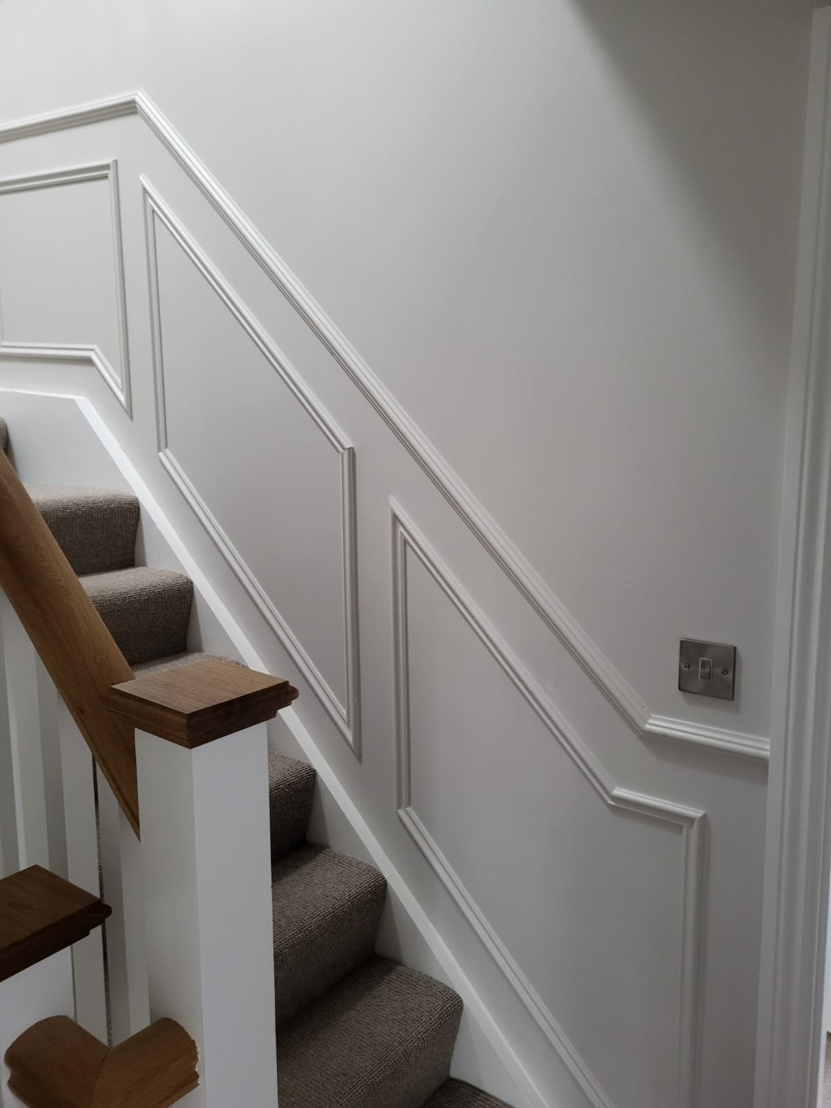 Staircase with white paneling and wooden handrail