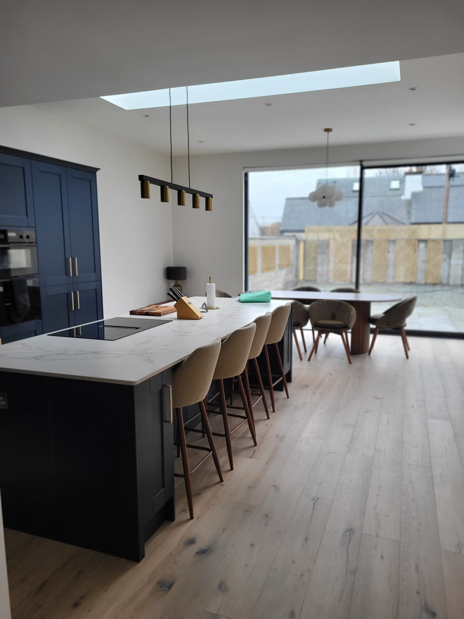 Modern kitchen with dark navy cabinetry, white marble countertops, glass pendant lights, and skylight