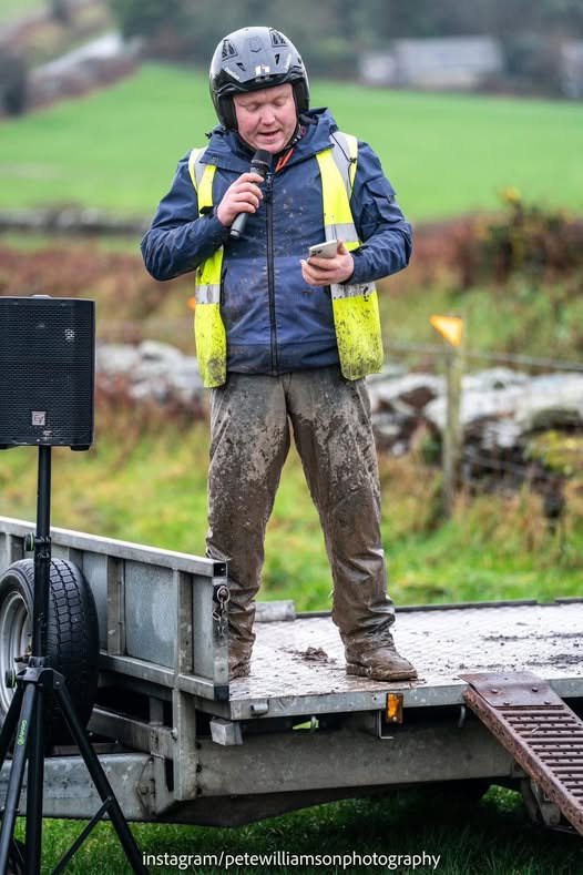 Tom Knight speaking at the charity motorcycle trial event wearing safety gear and holding a microphone