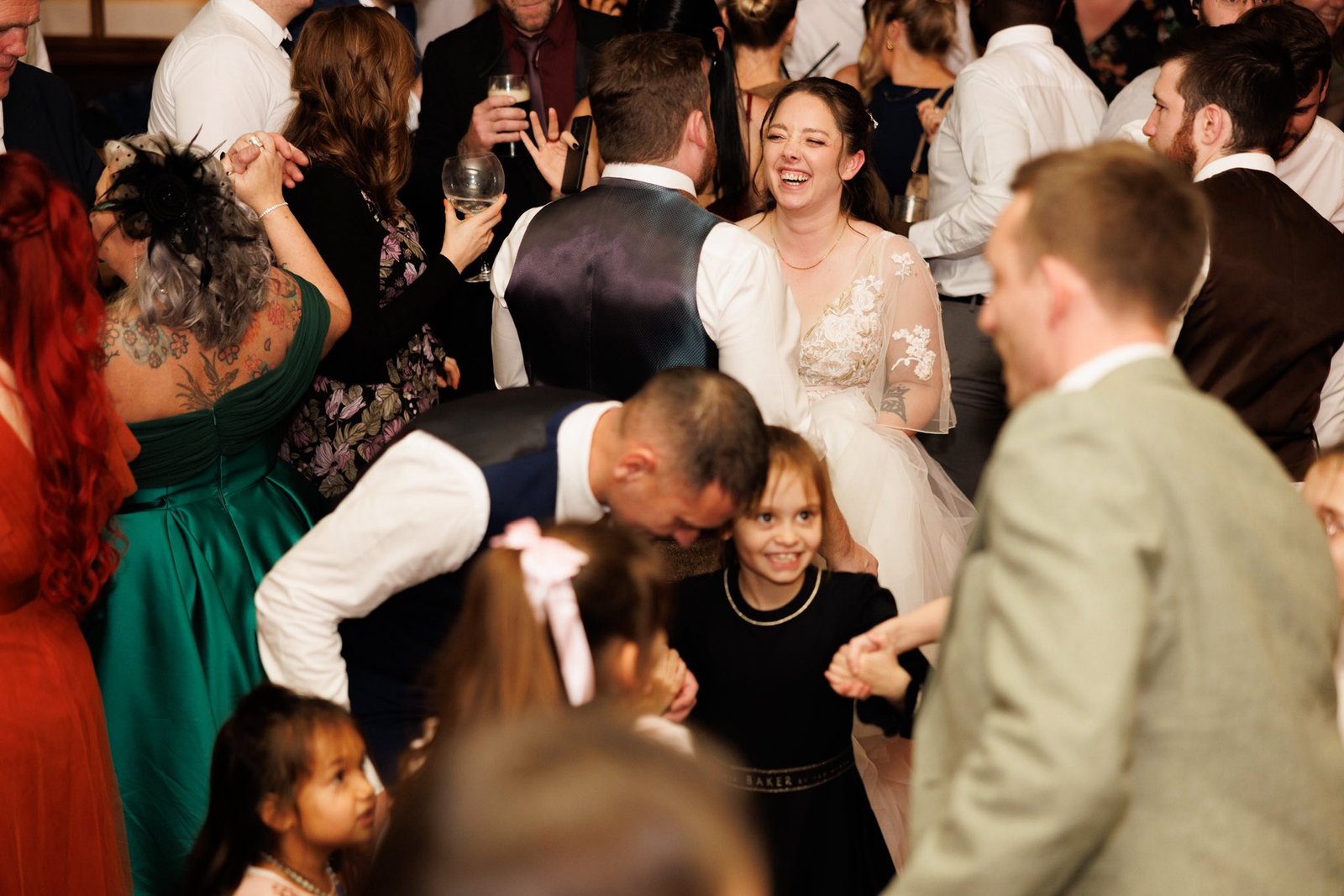 Wedding reception with guests dancing and celebrating, bride in white dress smiling, festive atmosphere with people in formal attire