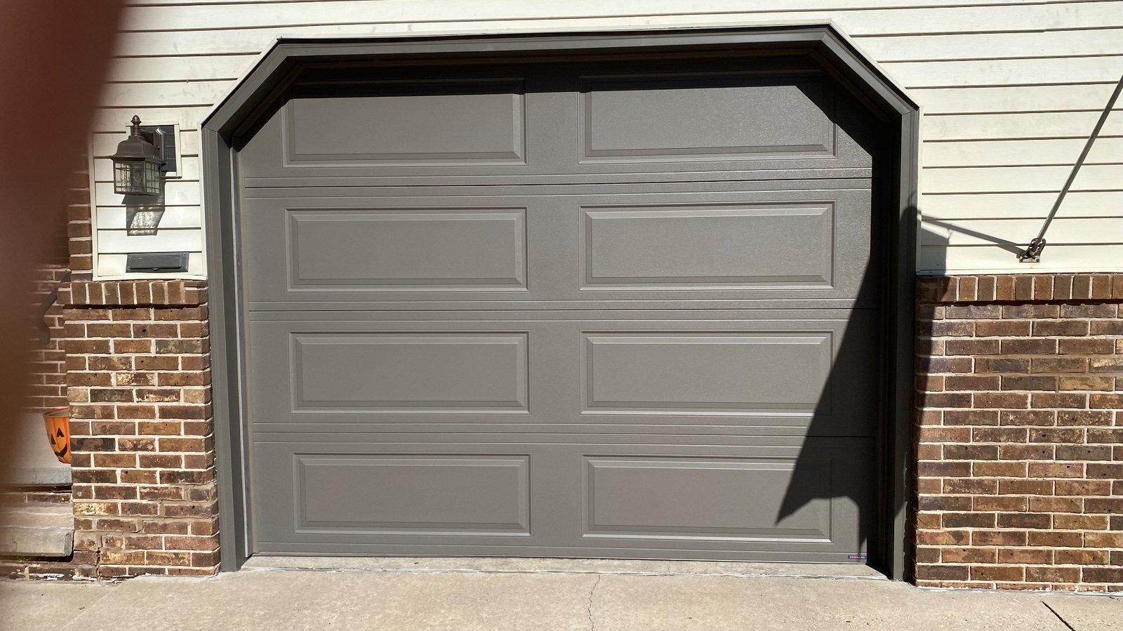 Gray garage door with bronze garage door trim, brick columns, and a wall lantern.