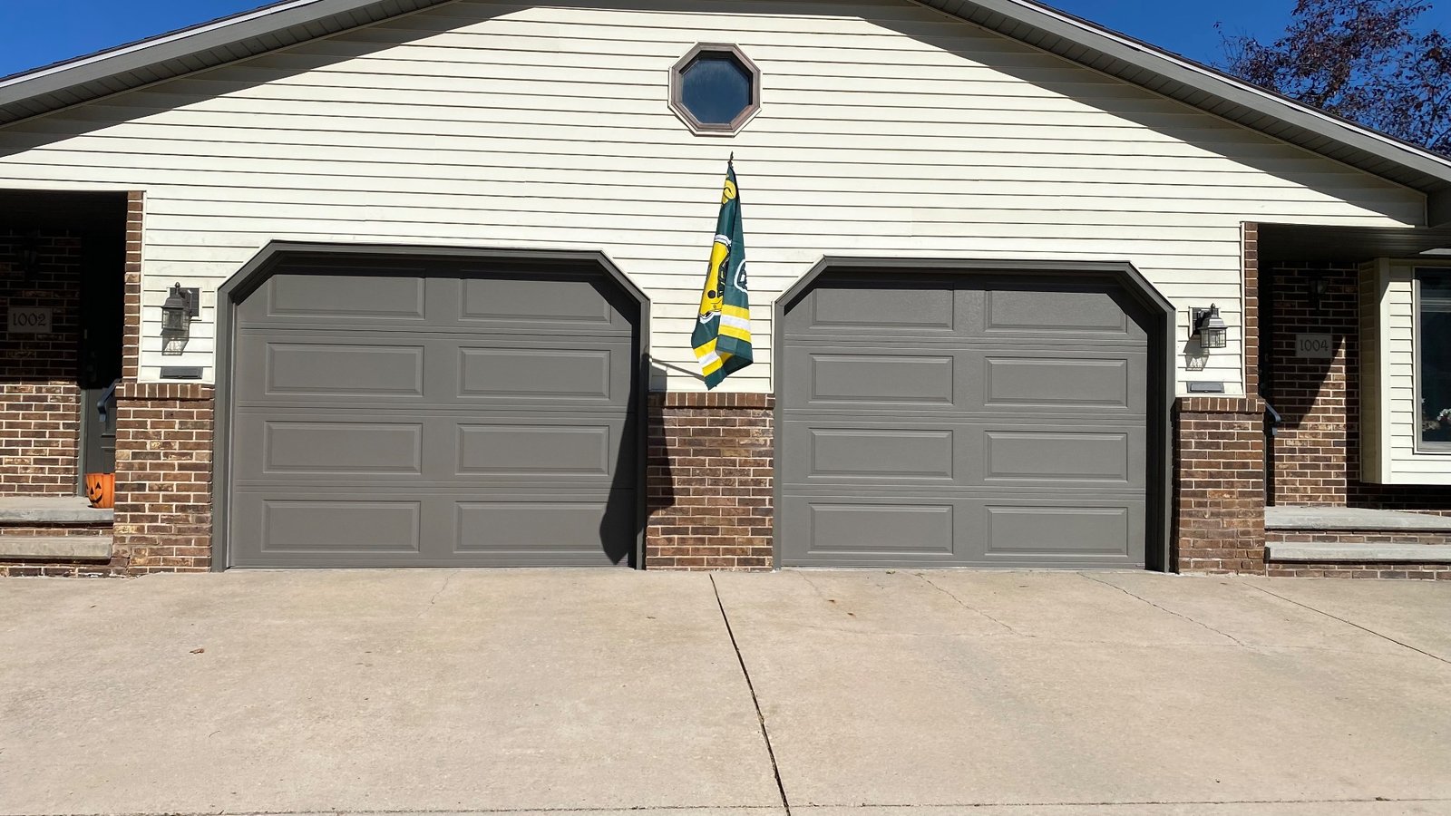 Two gray garage doors with bronze garage door trim, brick columns, and cream siding.