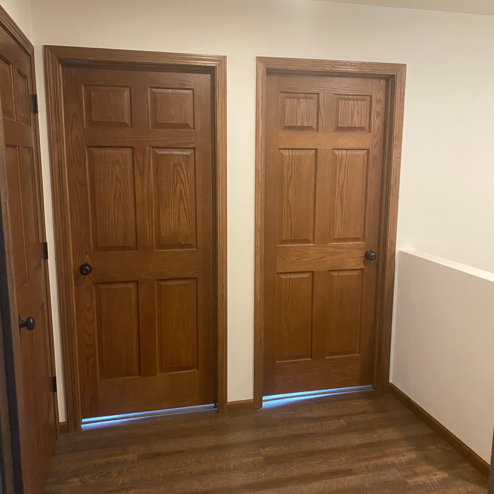Interior hallway with two six-panel stained wood doors and matching wood trim on hardwood flooring