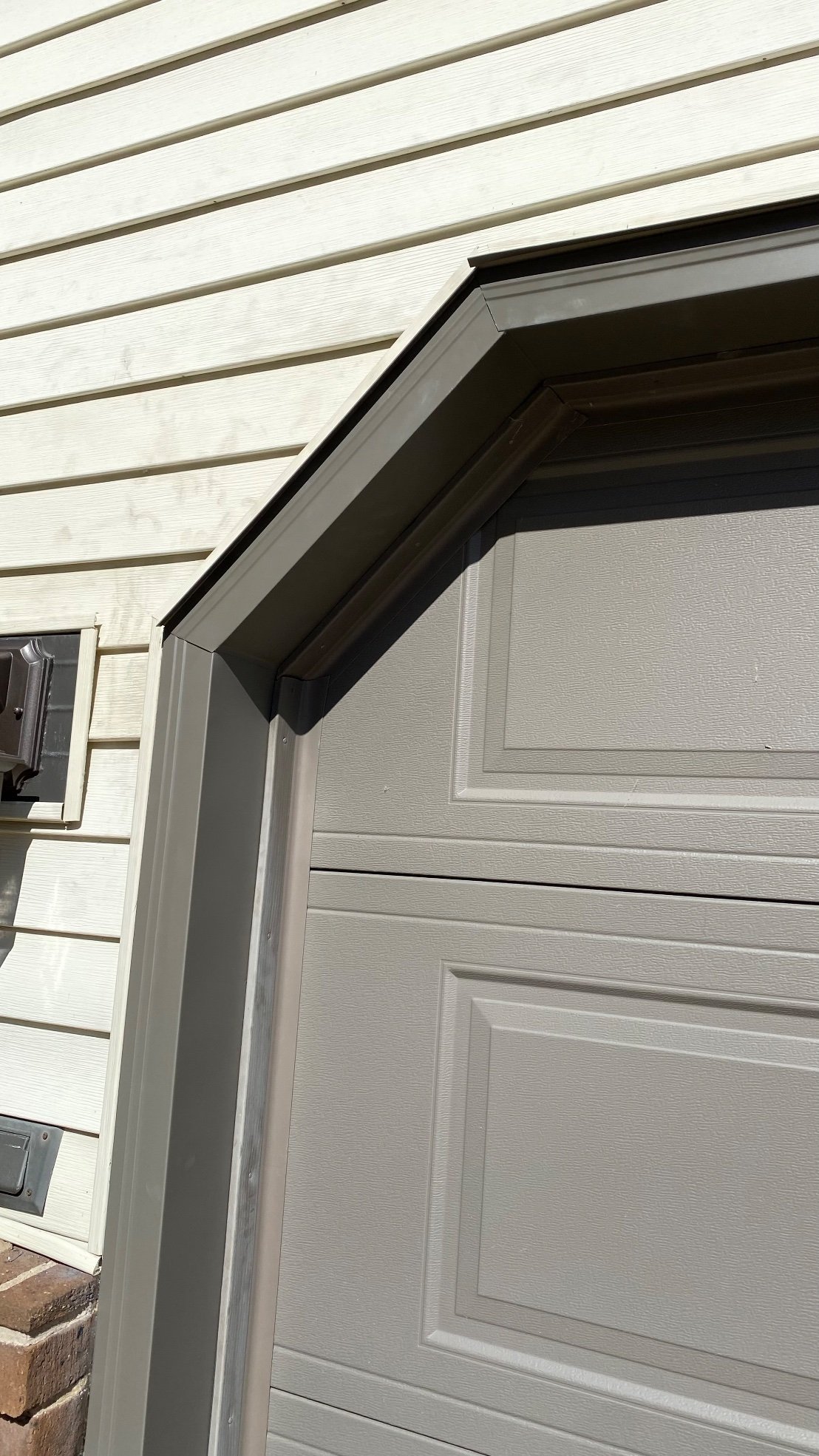 Close-up of bronze garage door trim at the upper left corner of a gray garage door.