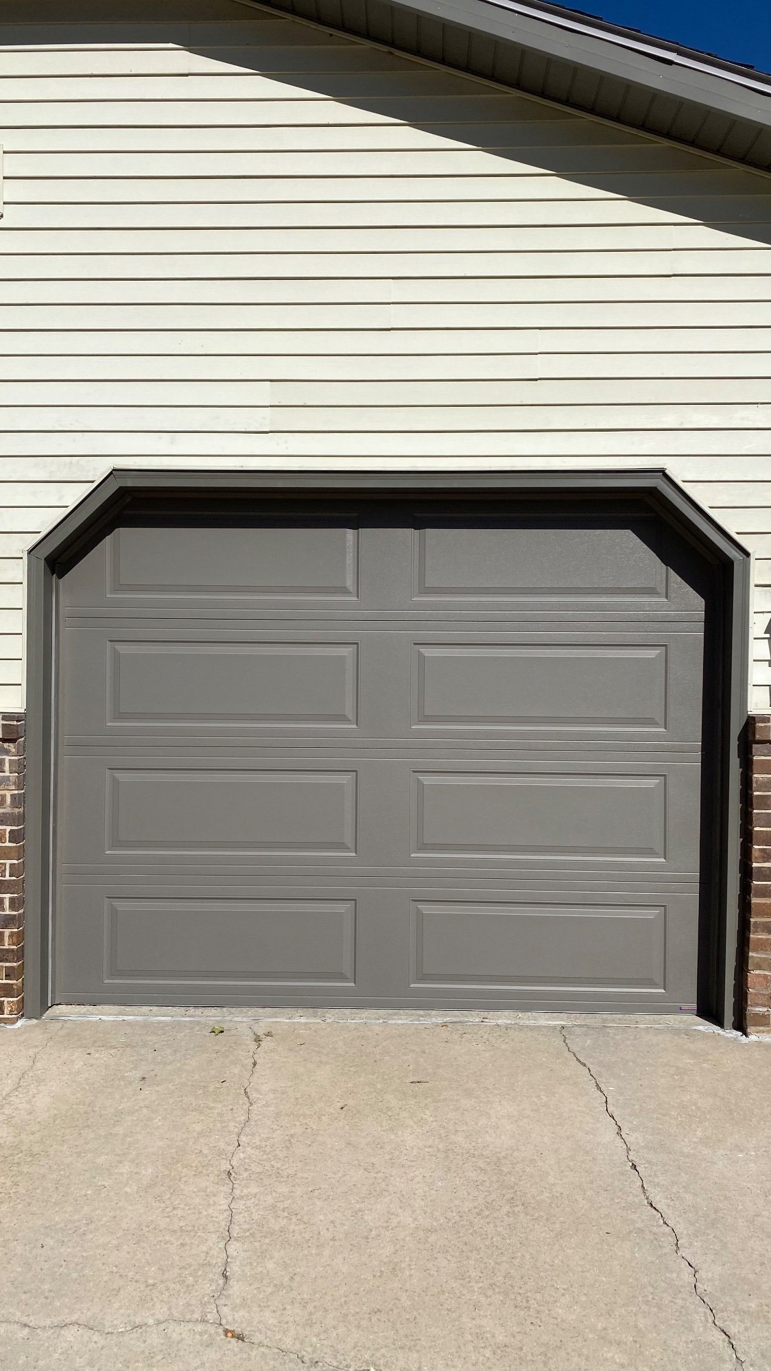 Bronze garage door trim around a gray raised-panel garage door on cream siding.