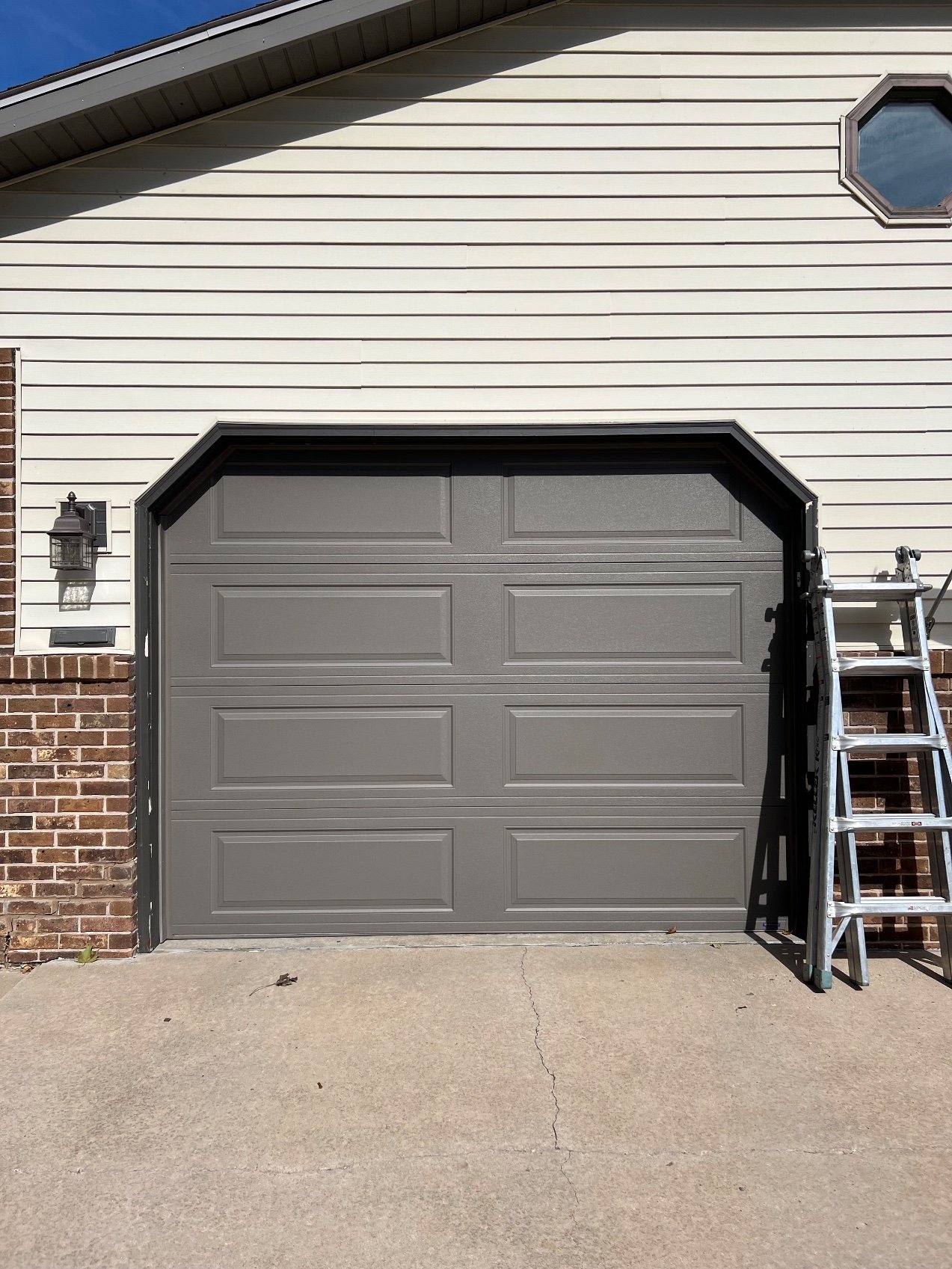 Gray garage door with bronze garage door trim and a ladder beside the opening.