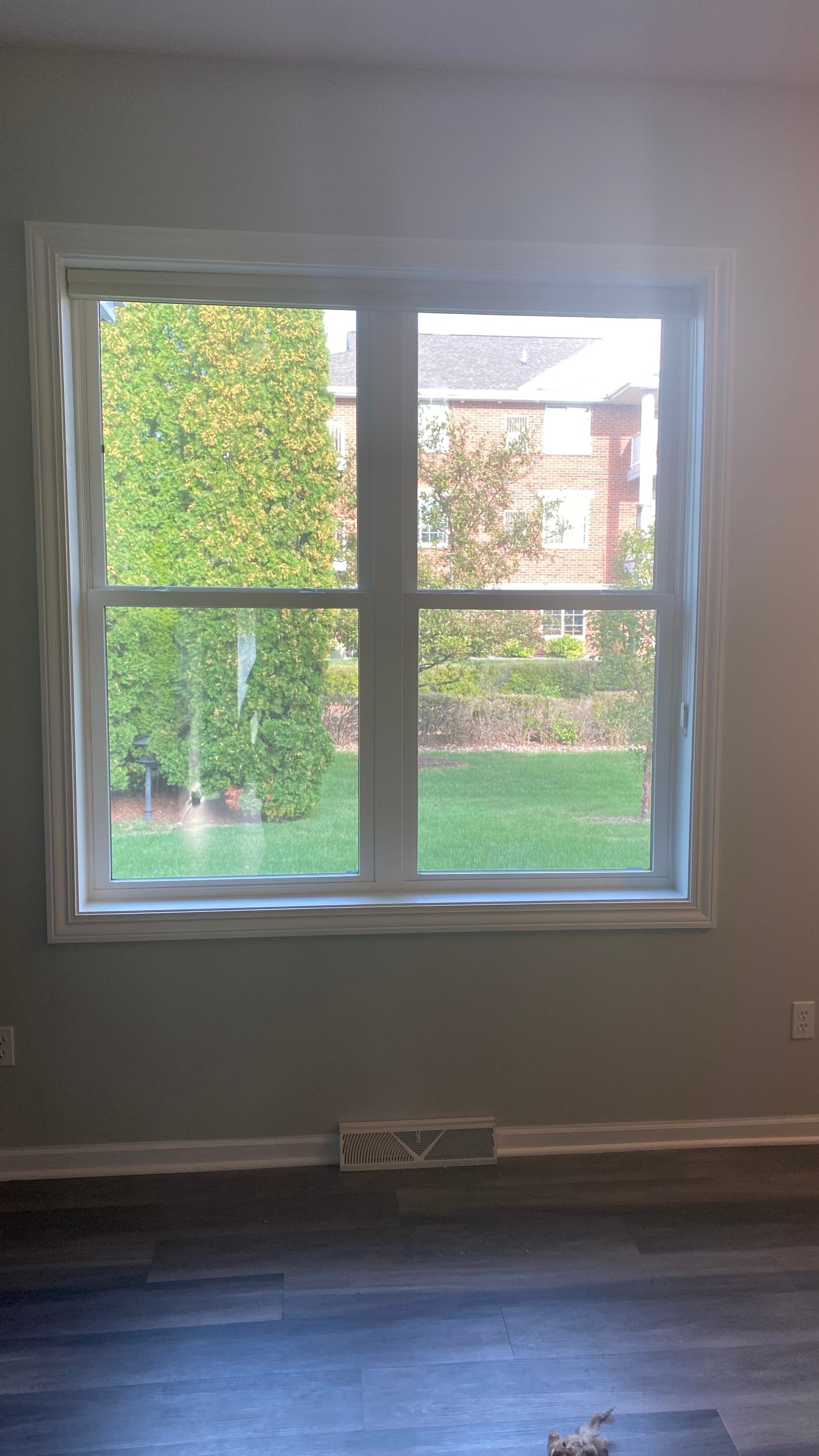 Large white four-lite interior window overlooking green lawn, trees, and a brick home exterior