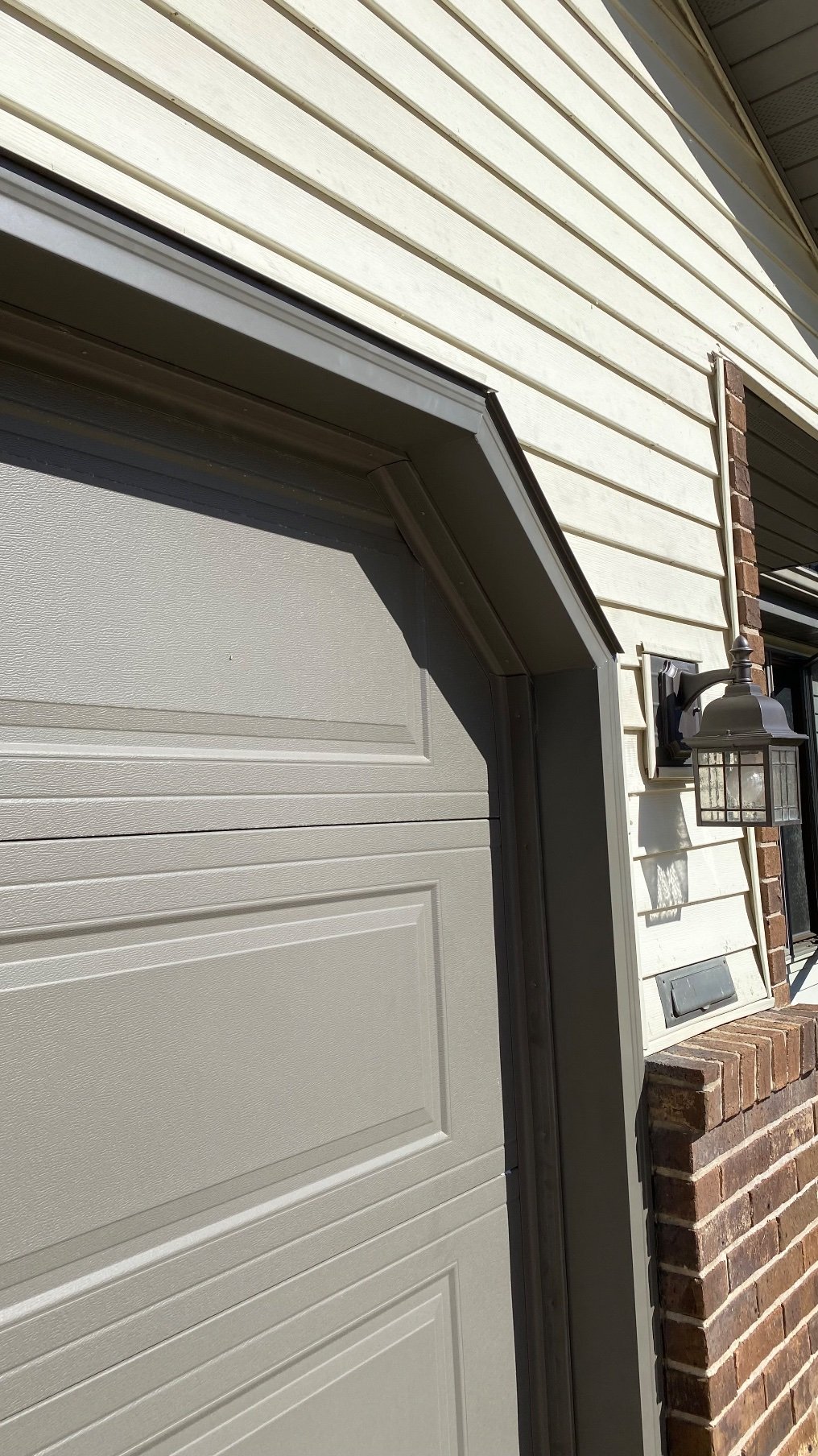 Bronze garage door trim beside a wall lantern and brick column.