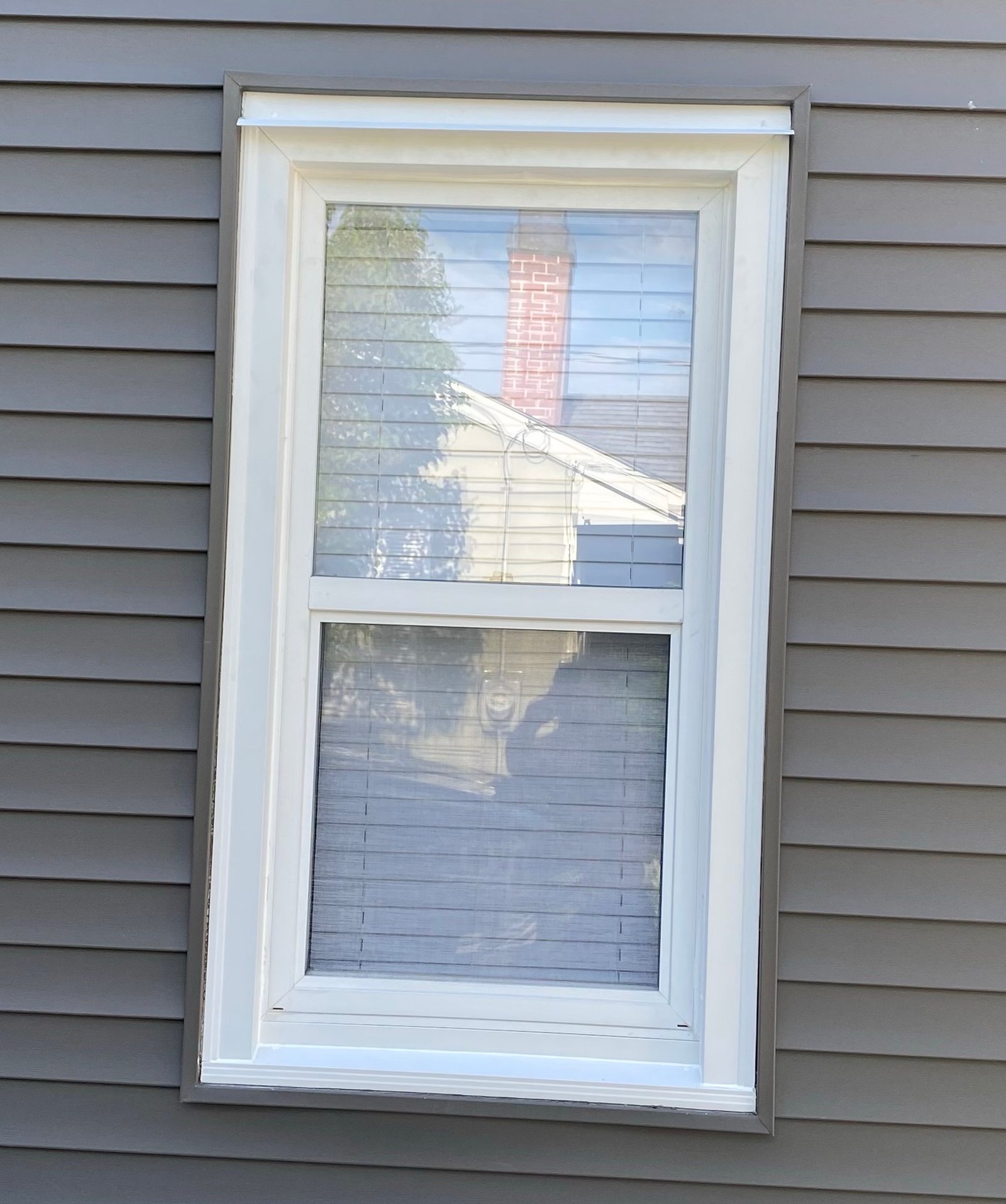 Exterior view of a white double-hung replacement window set in gray horizontal siding next to a utility meter