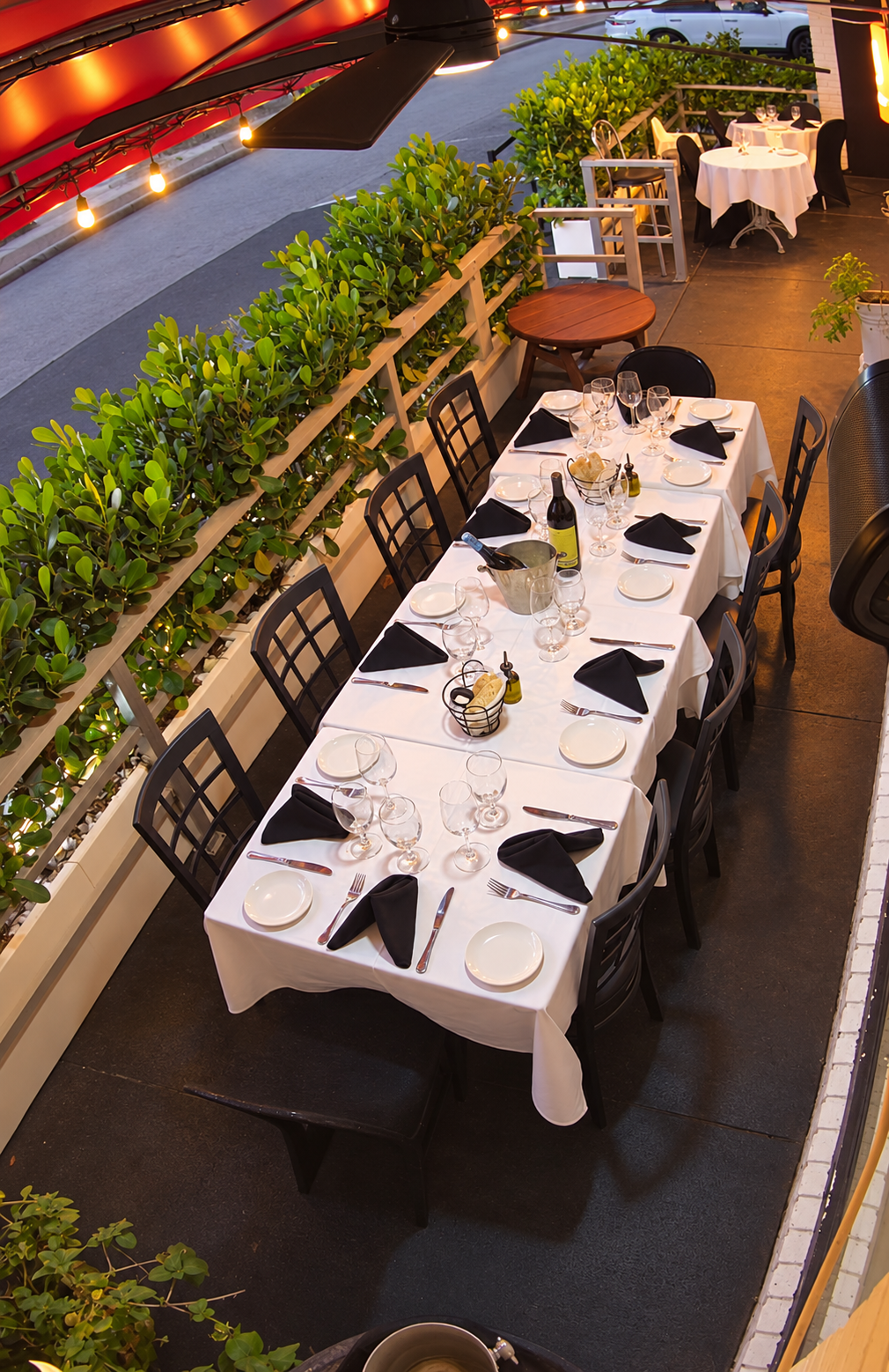 Long outdoor table set with white linen, black napkins and wine