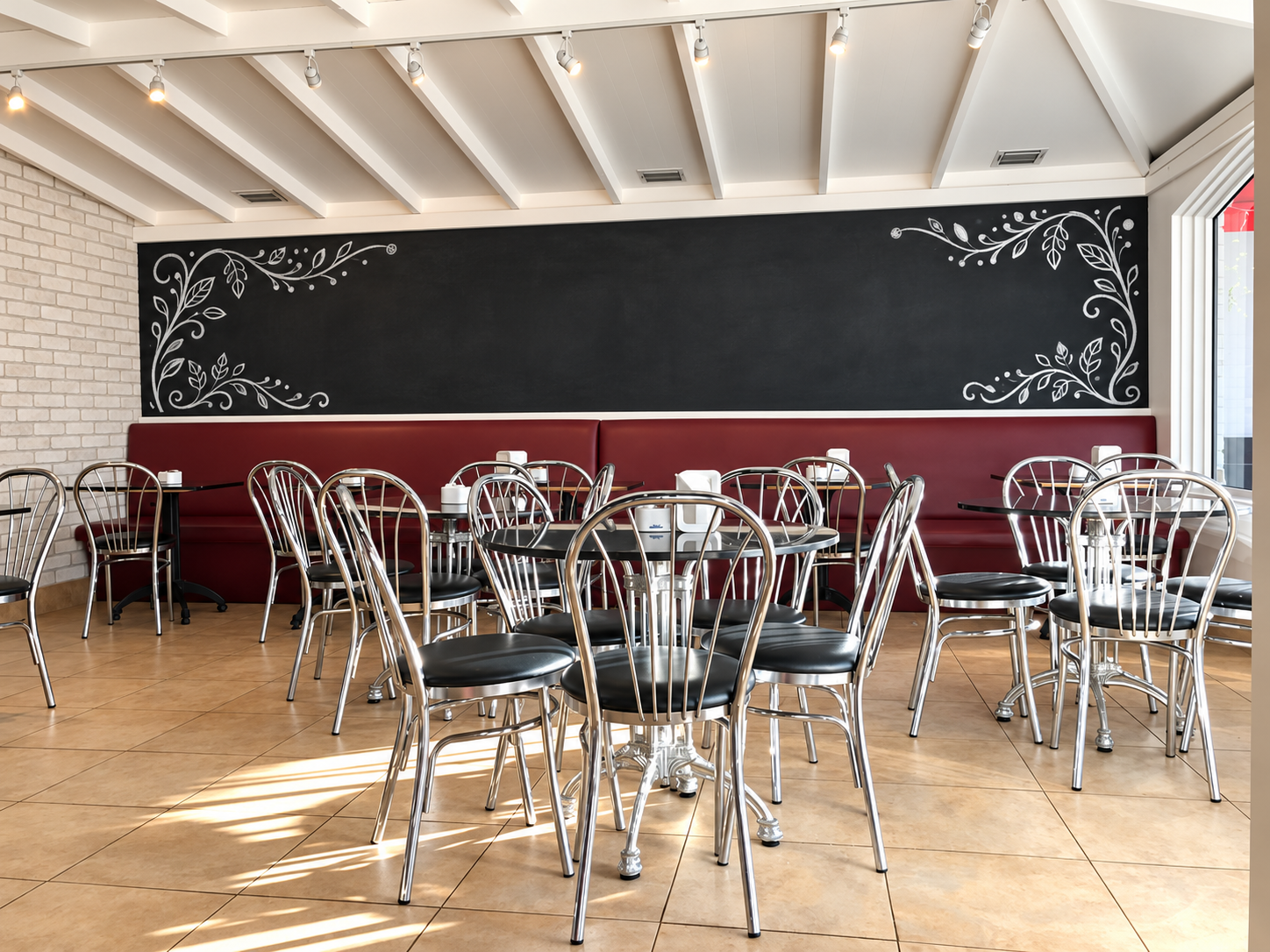 Dining room with red banquettes, chrome chairs and a floral chalkboard