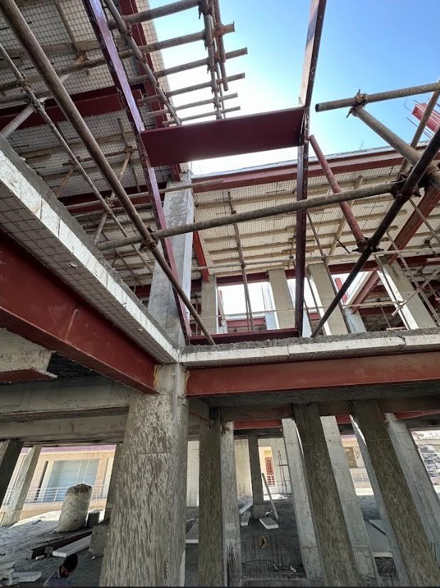 Looking up through red steel beams, concrete columns and scaffolding