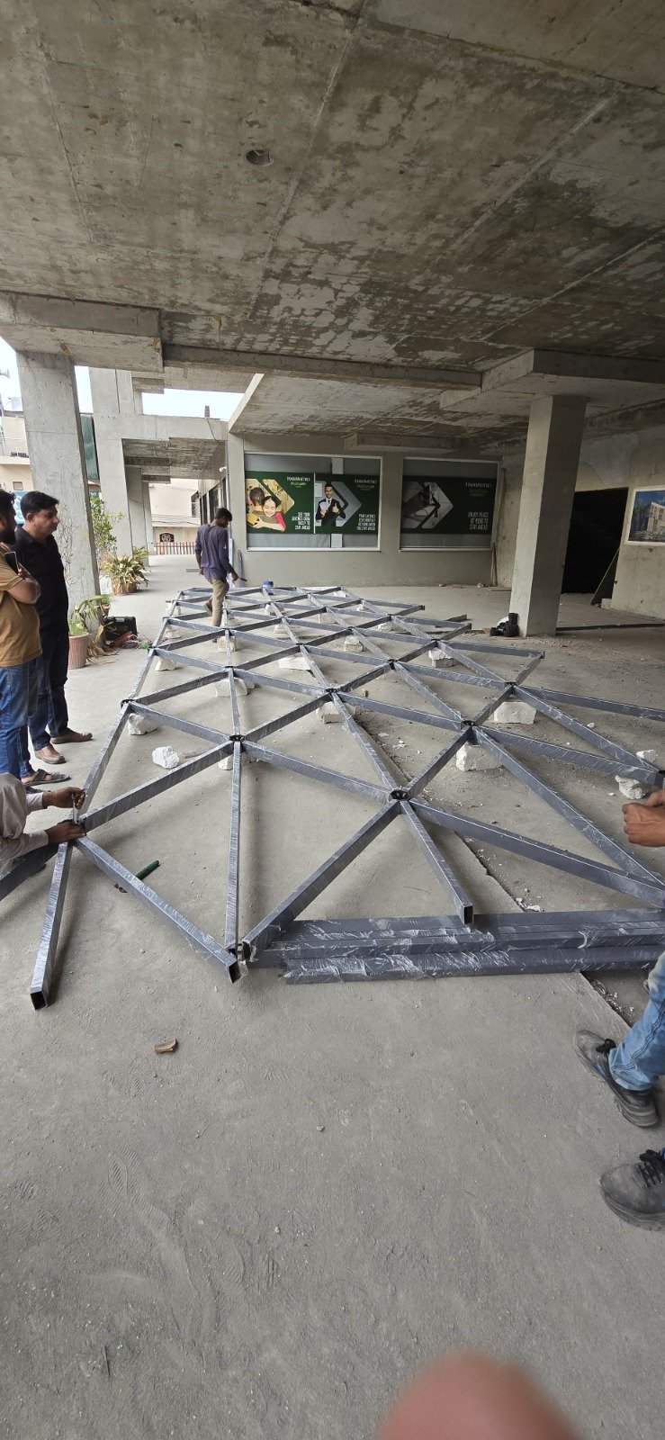 Steel triangular roof-frame sections arranged on the floor inside an unfinished building