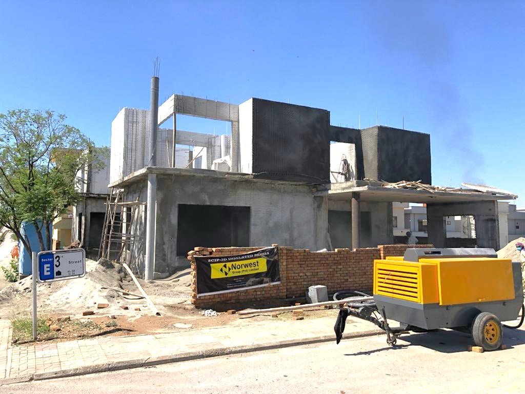 SCIP-3D insulated panel house with a Norwest site banner and compressor