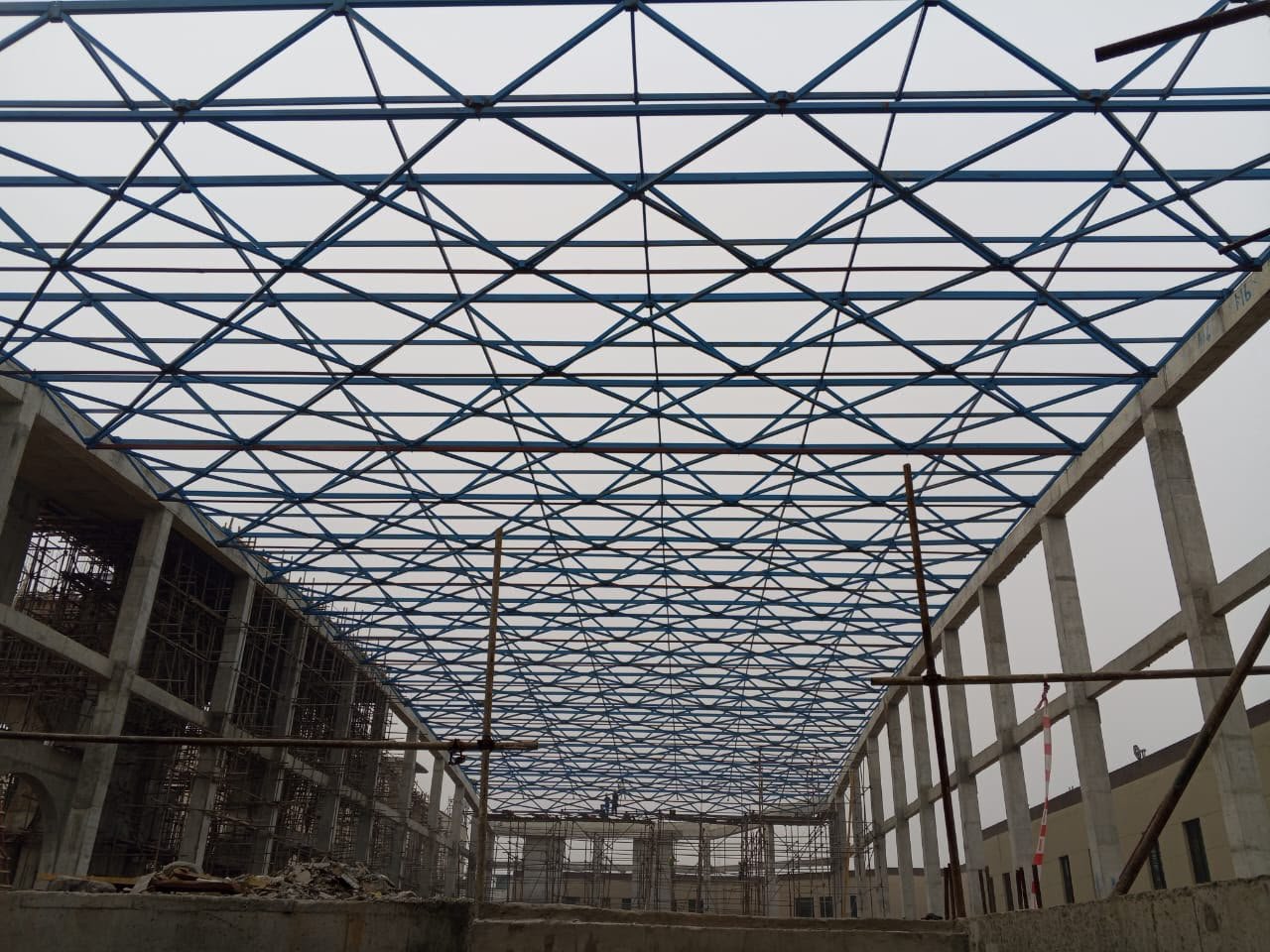 Looking along a blue steel lattice free-form roof between concrete columns