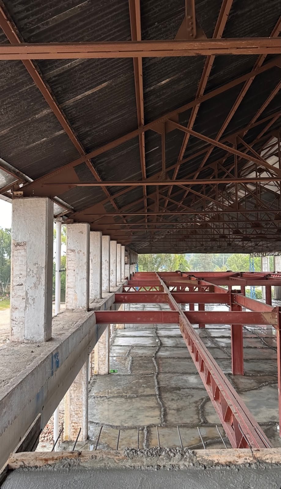 Red steel mezzanine beams and concrete columns under a steel roof