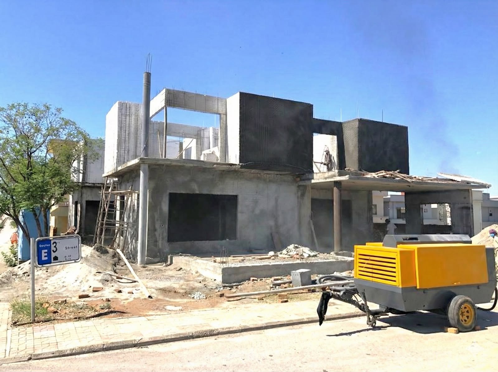 House frame with black rendered upper walls and a yellow compressor on site