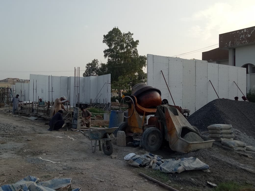 Concrete mixer and stacked cement bags beside insulated house wall panels