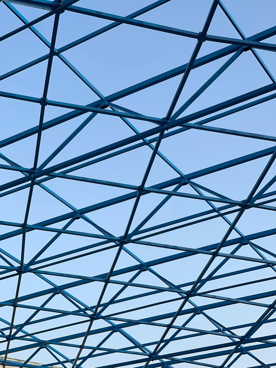 Close view of the blue steel free-form roof lattice against a clear sky