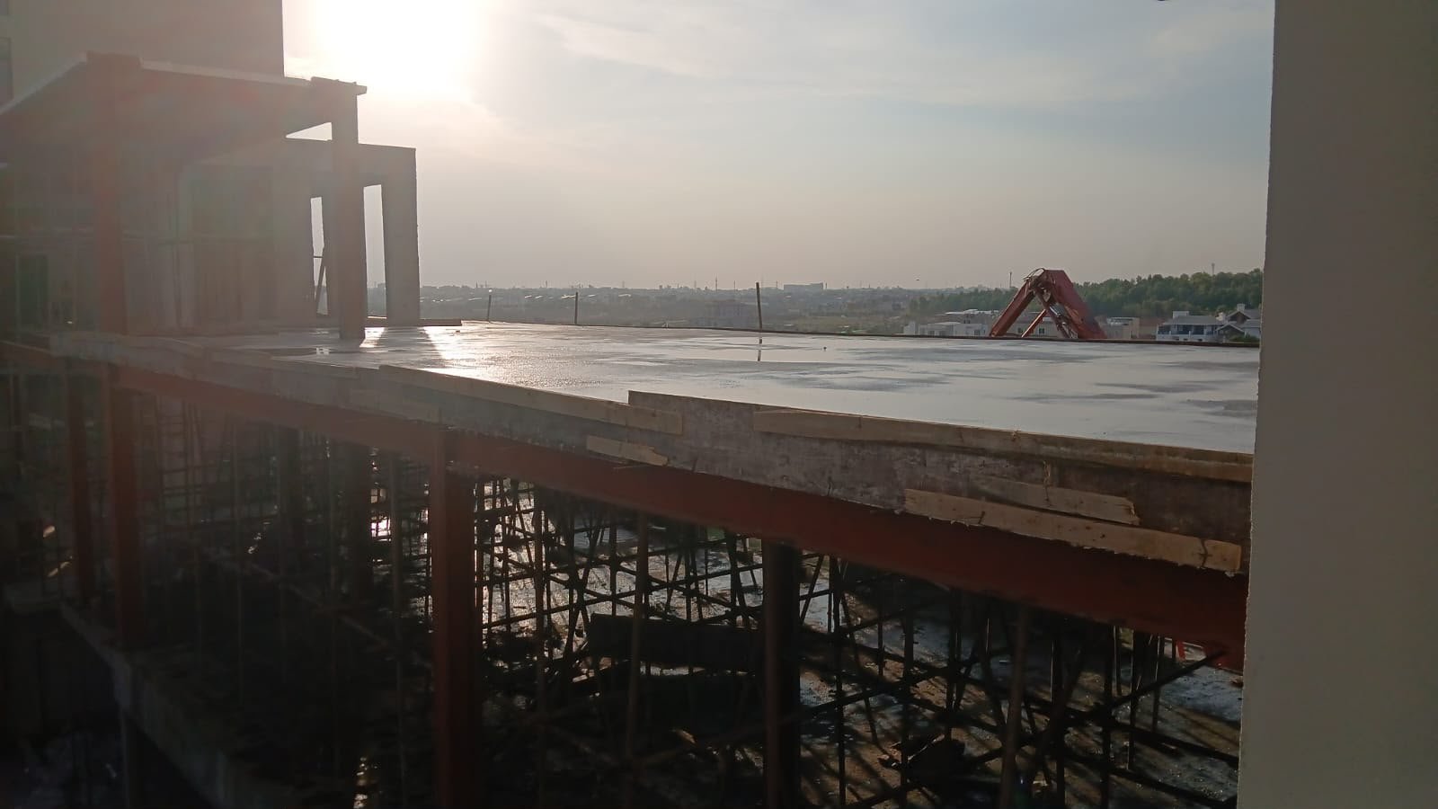 Freshly poured slab at sunset with scaffolding and a crane beyond