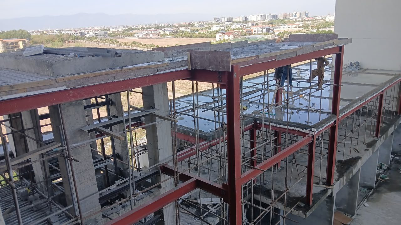 Multi-level red steel frame with a city skyline beyond the site