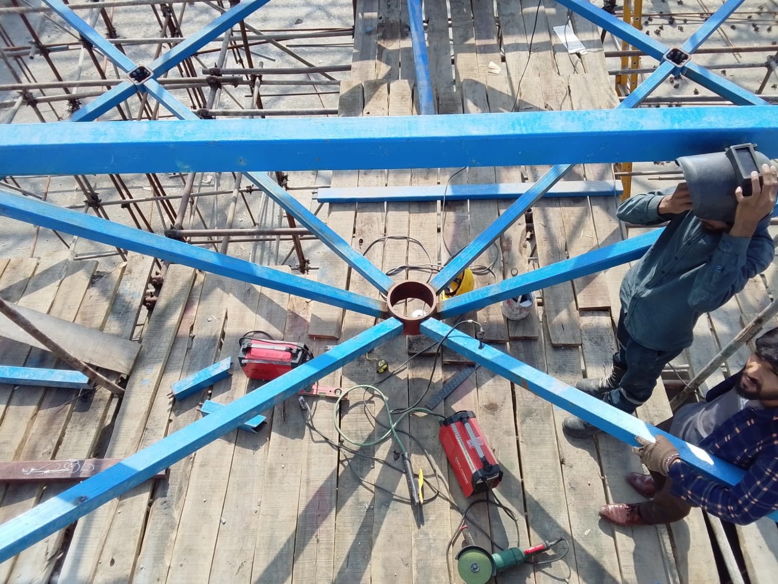 Welders working a central node on the blue steel free-form roof deck