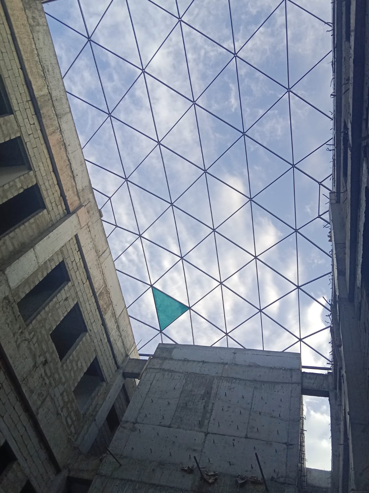 View upward through a triangulated roof lattice between concrete walls, with sky visible