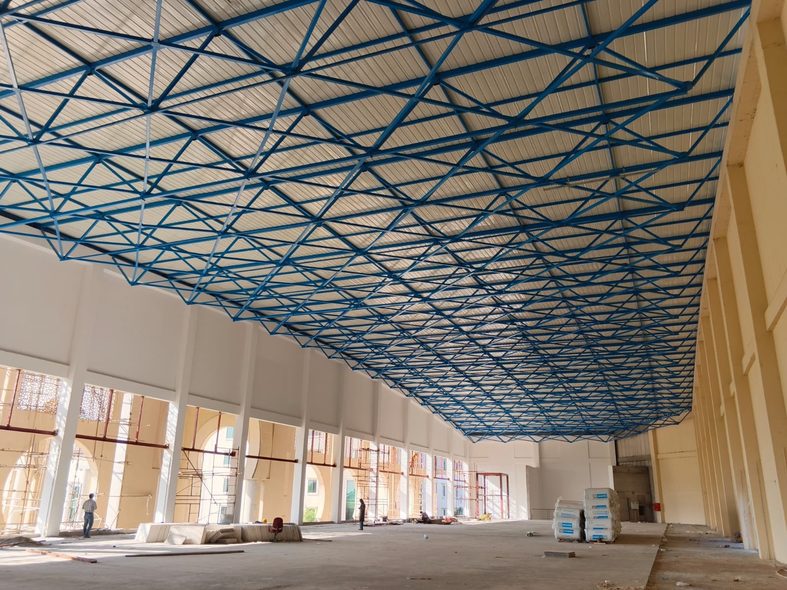 Blue steel roof lattice spanning a hall with arched windows and scaffolding along the wall