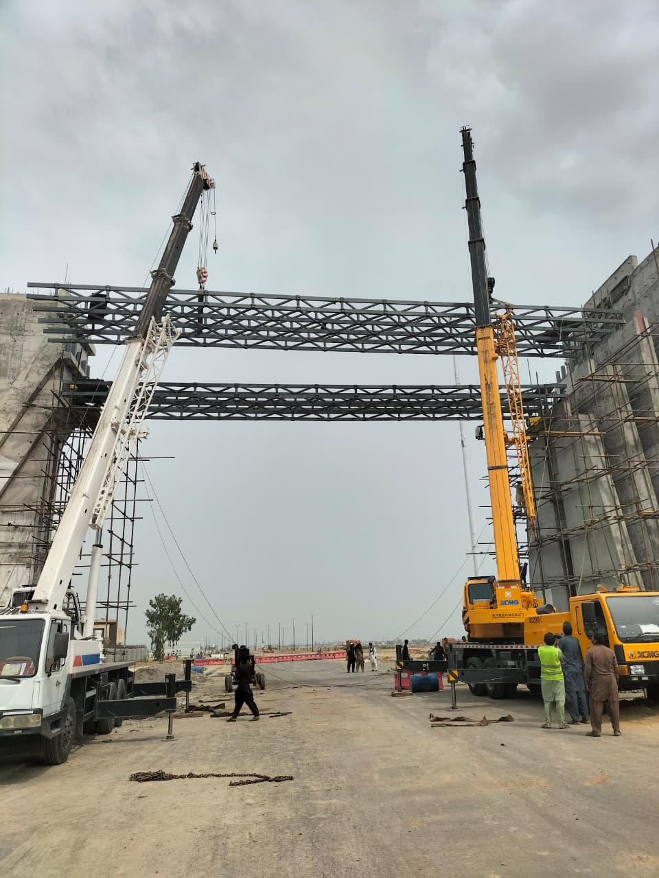 Grid shell gateway under construction with two cranes lifting lattice members, Lahore CBD
