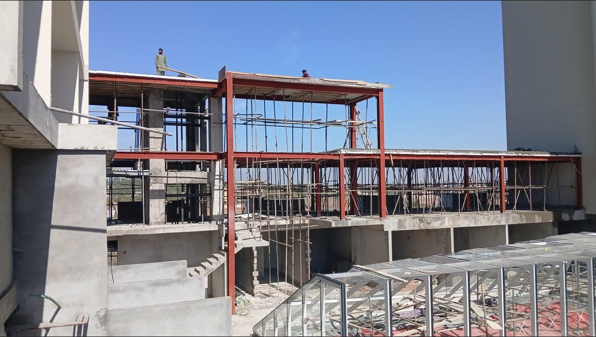 Workers on a red steel frame above a concrete stair and glass panels