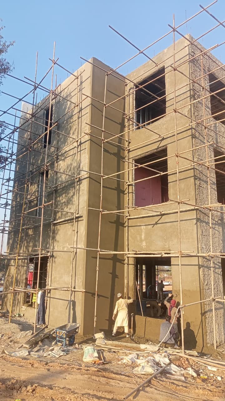 Workers plastering multi-story SCIP walls with bamboo scaffolding on a clear day in Rawalpindi