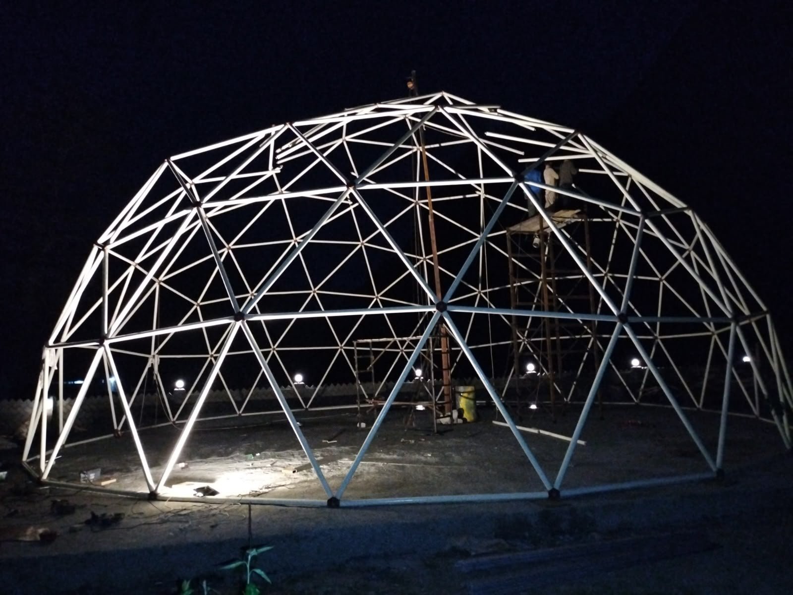 Event Dome frame lit at night with crew working from scaffolding