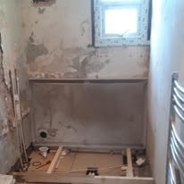 Bathroom renovation in progress with exposed construction, wooden framing, unfinished shower area