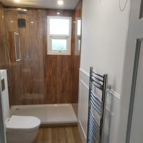 Completed modern bathroom with wood-look flooring, white subway tiles, black towel rail, gold fixtures, professional finish