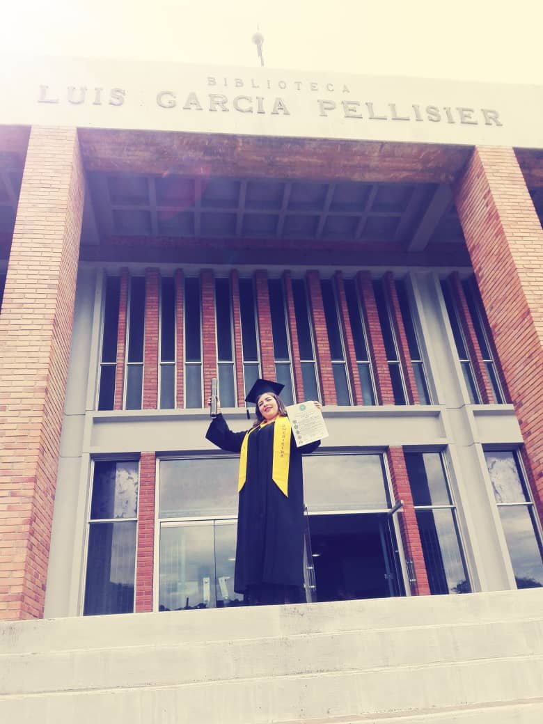 Logro Académico: Dra. Katherine López en toga y birrete recibiendo diploma frente a la Biblioteca Luis García Pellisier