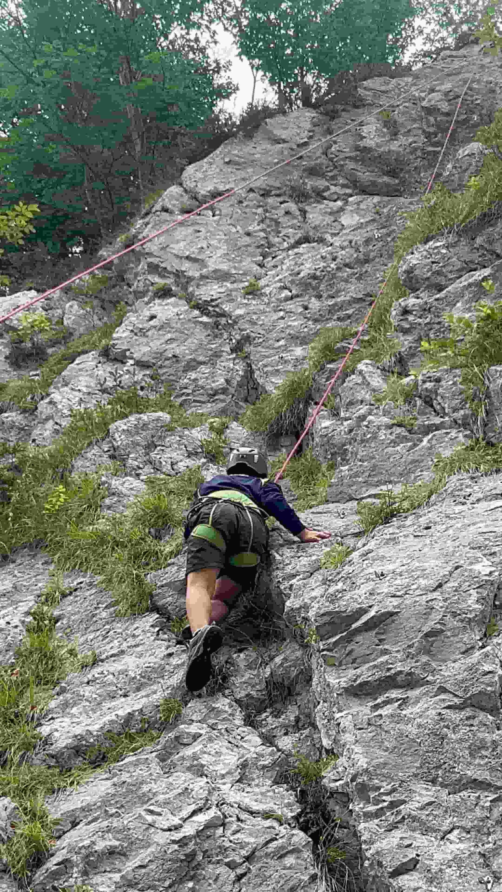 Un ragazzo con casco e imbrago durante l'arrampicata sulla parete di roccia