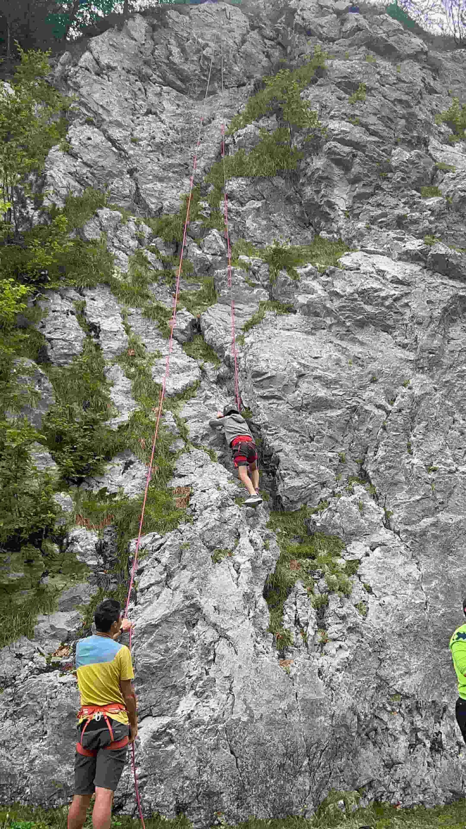 Arrampicata in corda doppia con l'istruttore che assicura dalla base