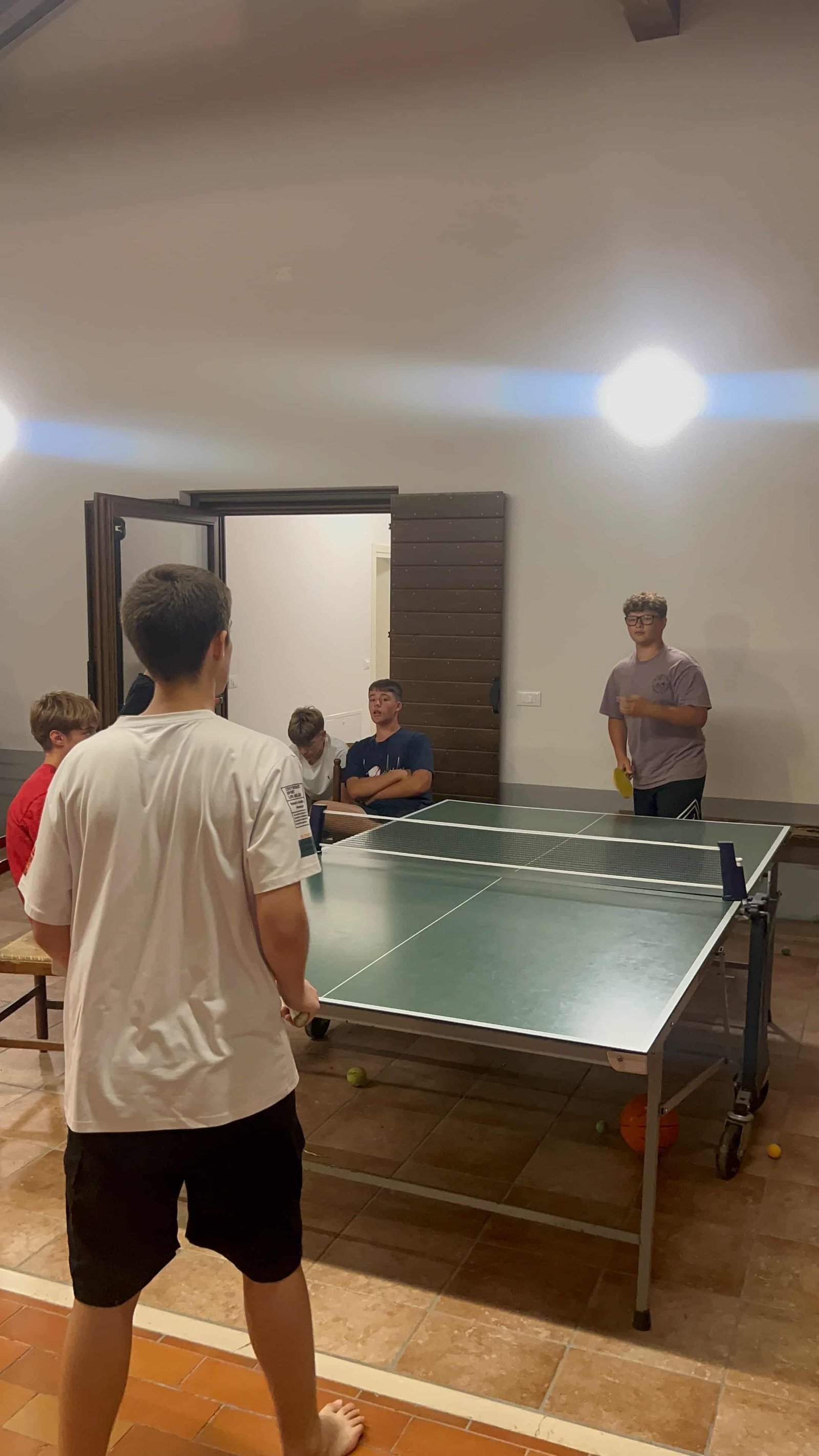 Partita di ping pong nel salone del camp con i compagni a bordo tavolo