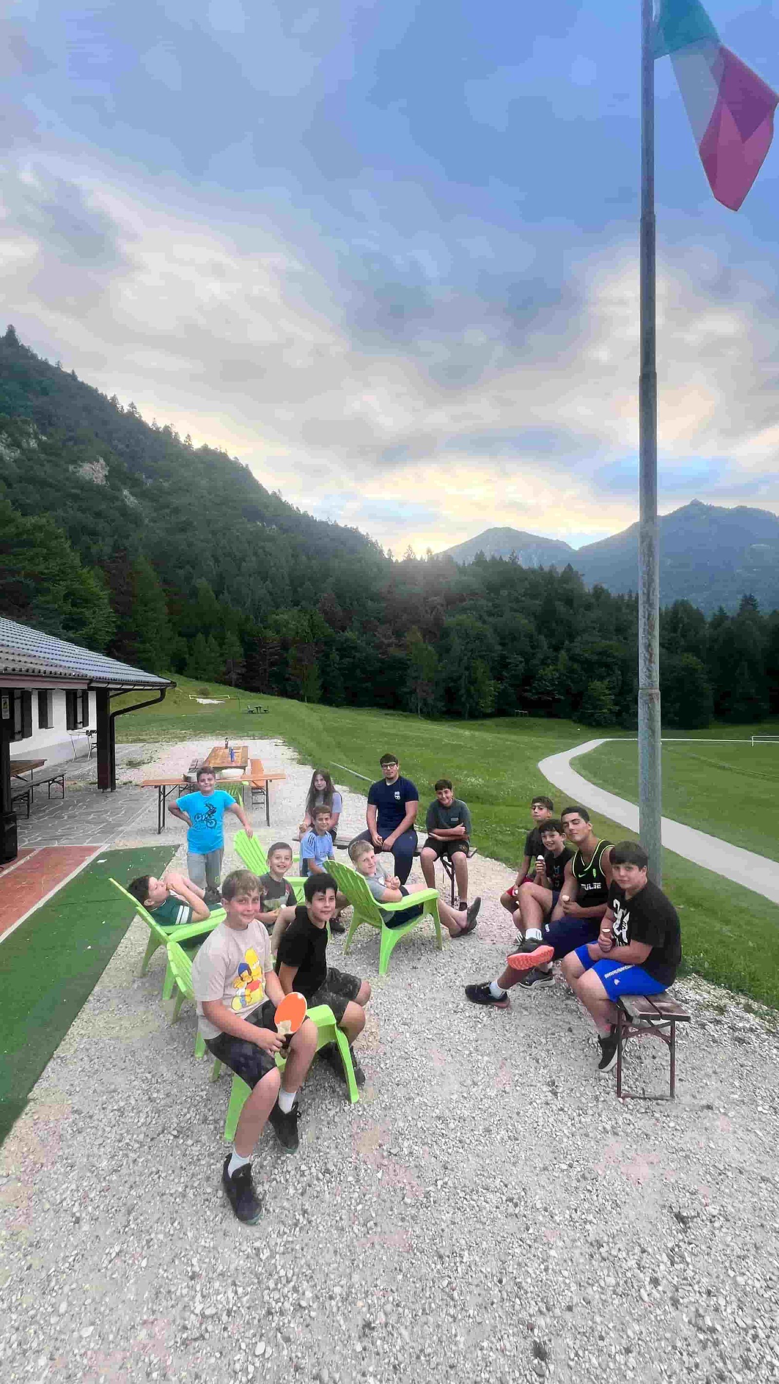 Il gruppo seduto sulle sedie verdi davanti alla bandiera e alla valle