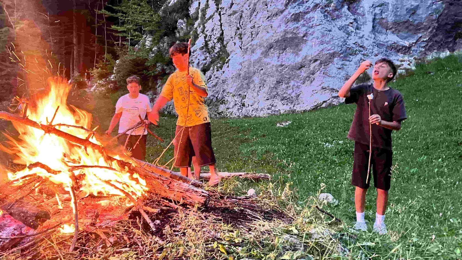 Ragazzi che arrostiscono salsicce sul fuoco davanti alla parete di roccia