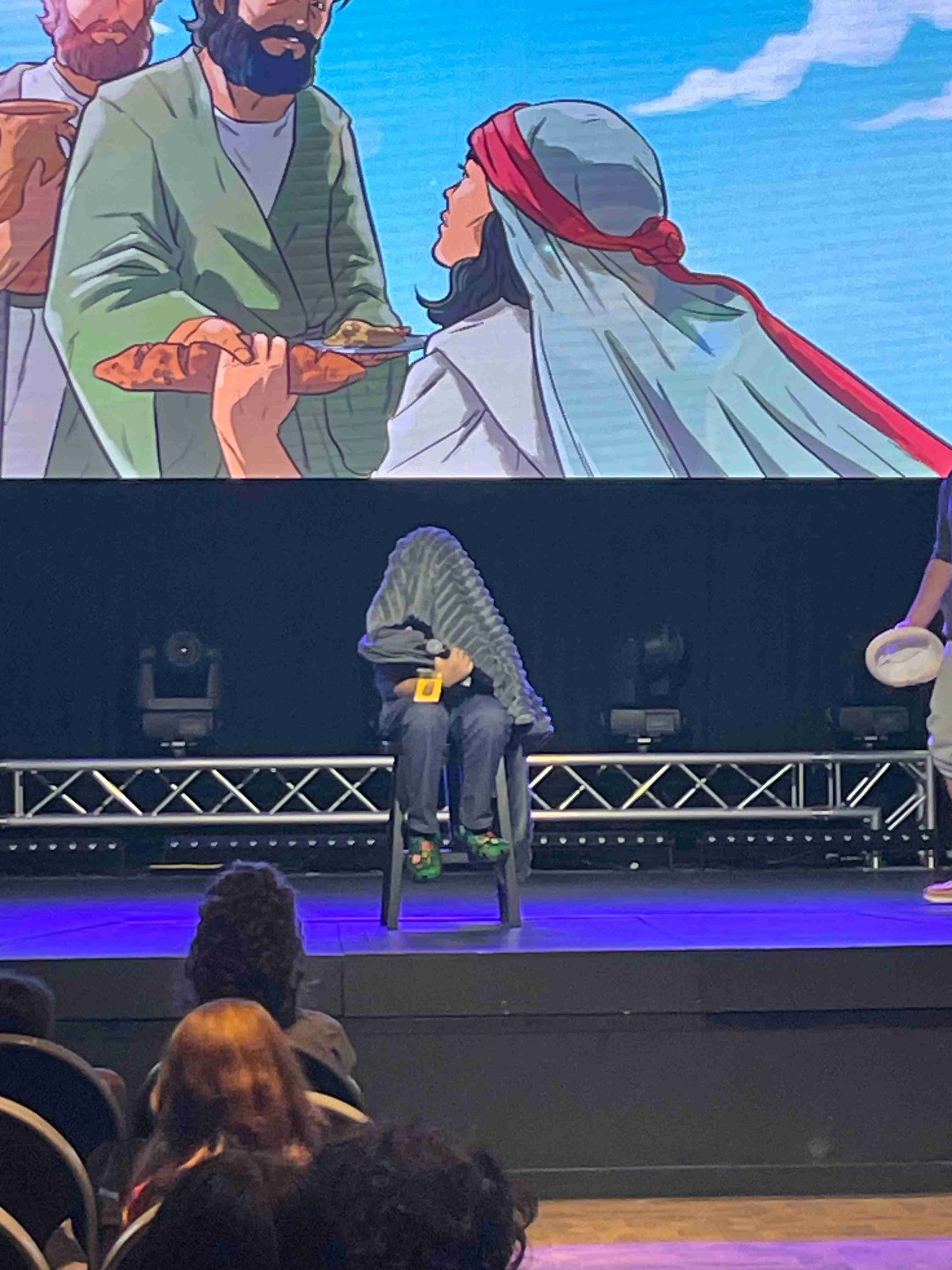 Youth skit on stage with person under blanket