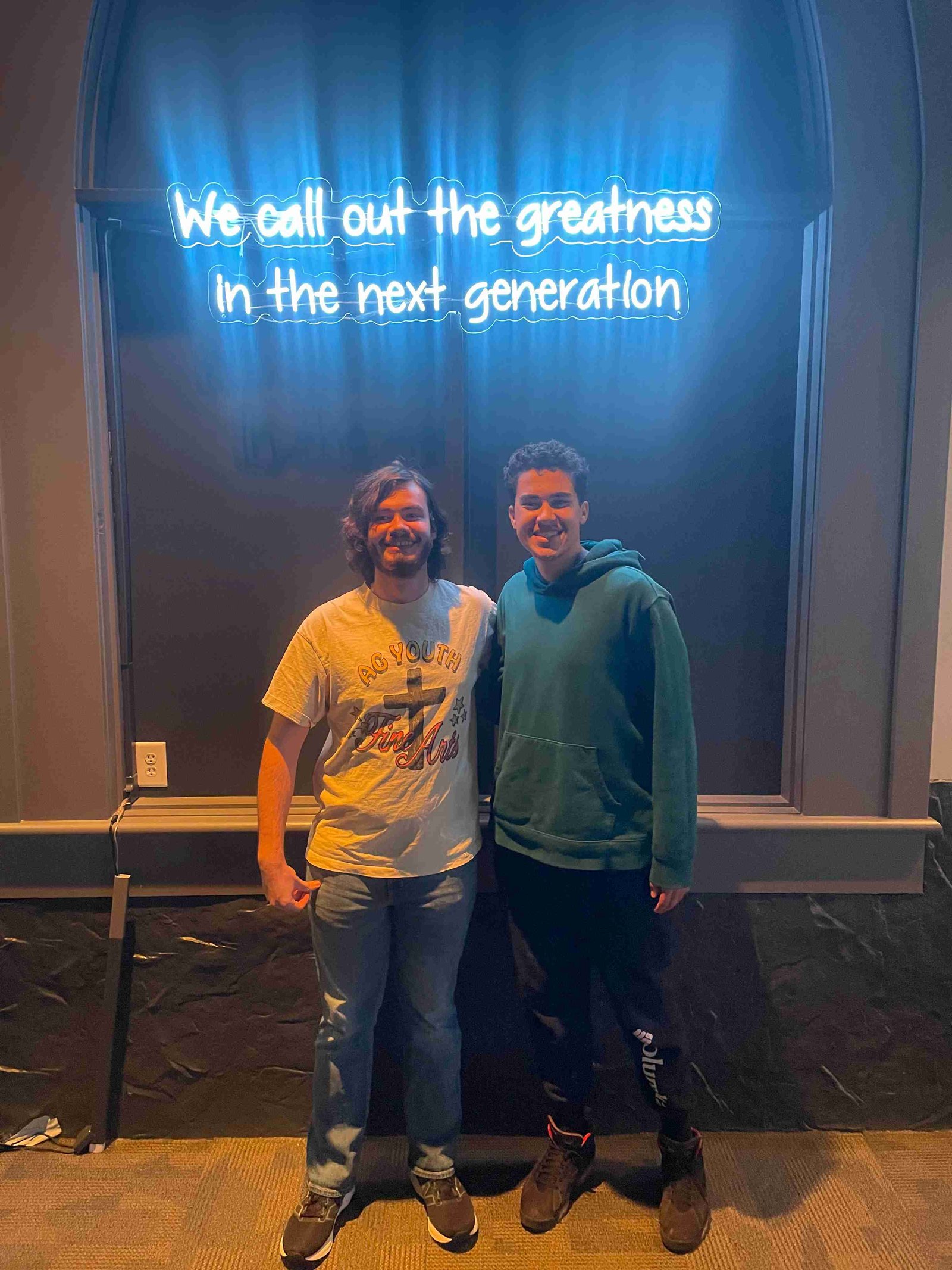 Two young men standing under a neon sign