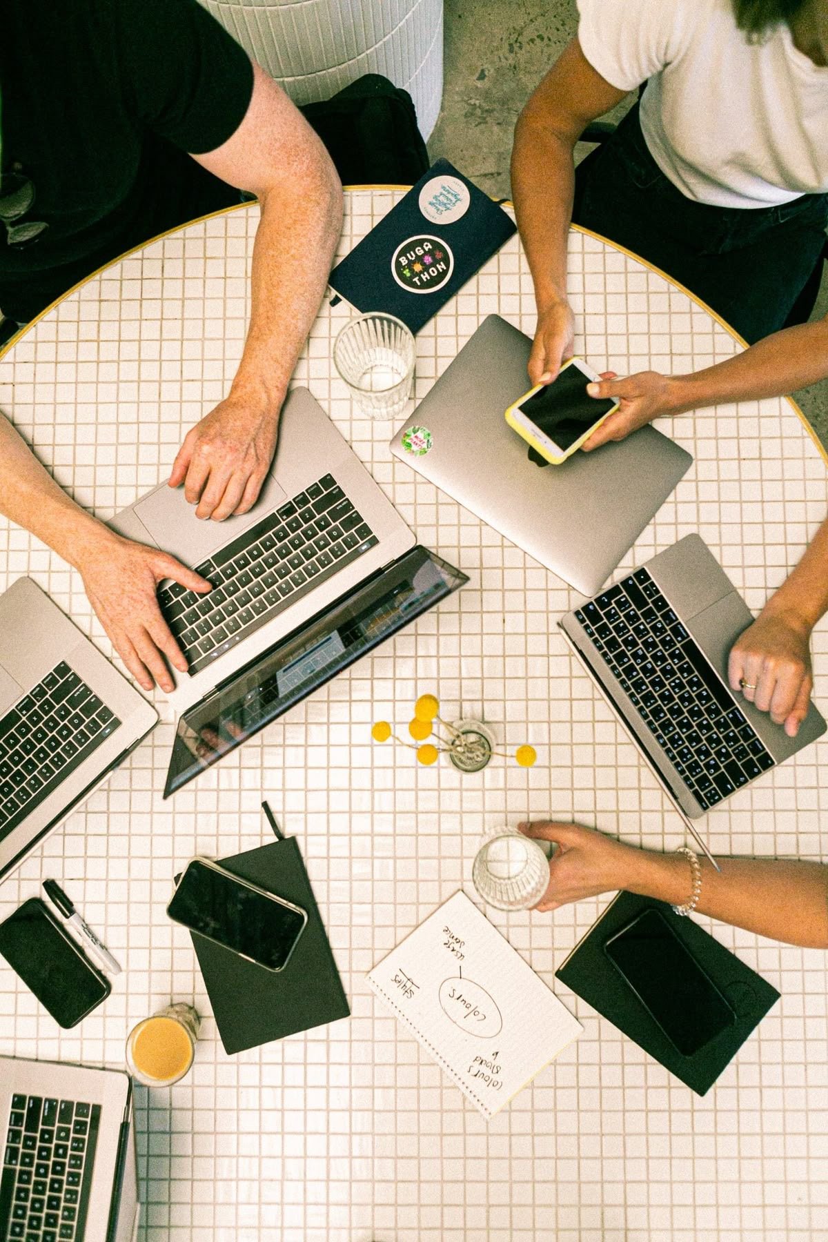 A team collaborates around laptops and notes at a tiled table.