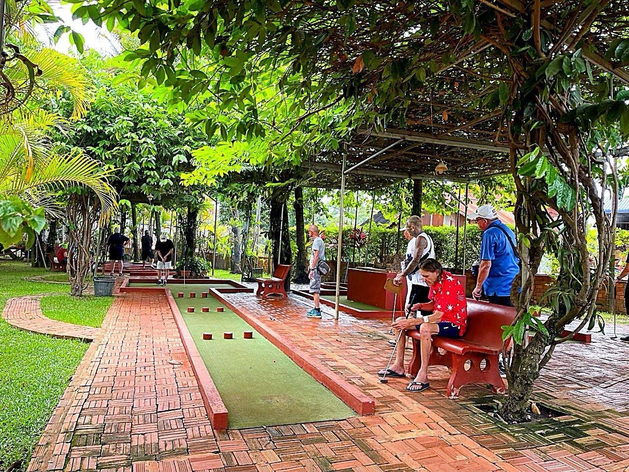 Happy guests playing mini golf under lush garden vines and trees